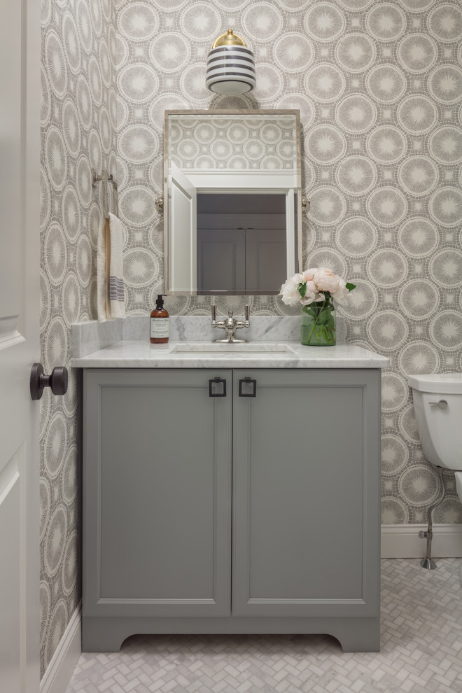 This is an example of a beach style powder room in Boston with grey cabinets, marble floors, an undermount sink, marble benchtops, recessed-panel cabinets, multi-coloured walls and white benchtops.