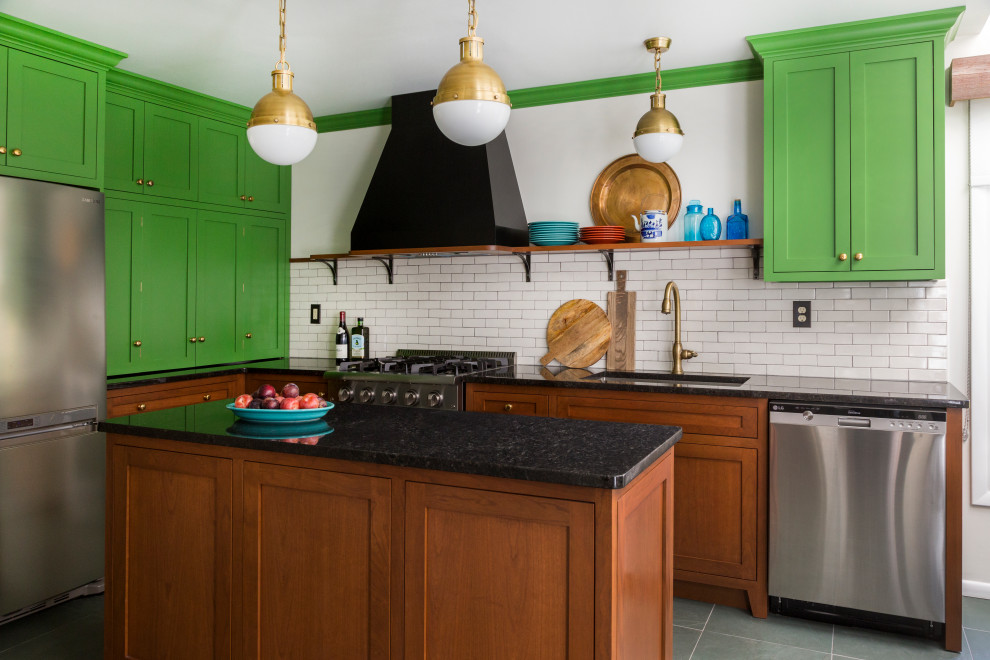 This is an example of a mid-sized eclectic l-shaped eat-in kitchen in Philadelphia with an undermount sink, shaker cabinets, green cabinets, granite benchtops, white splashback, ceramic splashback, stainless steel appliances, slate floors, with island, green floor and black benchtop.