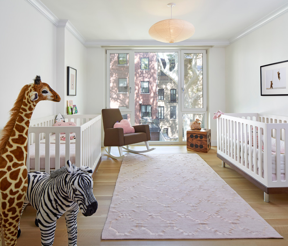Photo of a transitional nursery for girls in New York with white walls and light hardwood floors.
