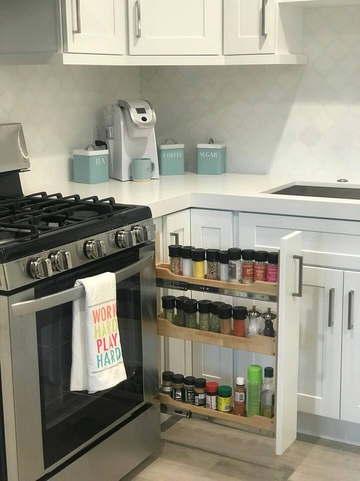 Inspiration for a mid-sized beach style u-shaped eat-in kitchen in Orange County with an undermount sink, shaker cabinets, white cabinets, quartz benchtops, white splashback, marble splashback, stainless steel appliances, porcelain floors, a peninsula, brown floor and white benchtop.
