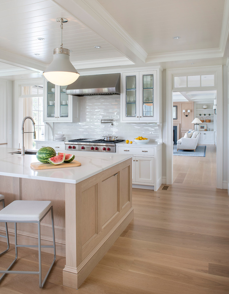 Inspiration for a beach style kitchen in Providence with an undermount sink, recessed-panel cabinets, white cabinets, white splashback, subway tile splashback, stainless steel appliances, medium hardwood floors, with island, brown floor, white benchtop and timber.