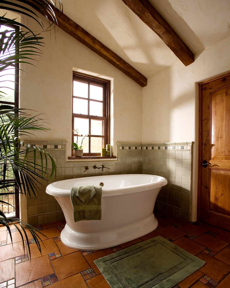 This is an example of a large master bathroom in Santa Barbara with a freestanding tub, terra-cotta floors and beige walls.