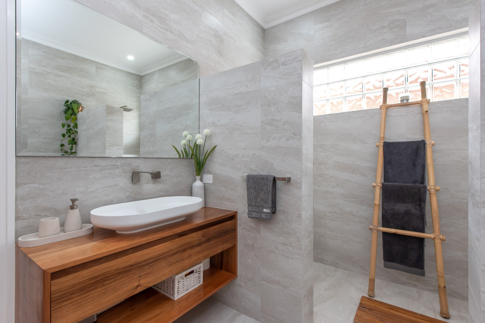 This is an example of a contemporary bathroom in Perth with medium wood cabinets, a drop-in tub, an open shower, gray tile, ceramic tile, ceramic floors, a vessel sink, wood benchtops, grey floor, a single vanity and a floating vanity.