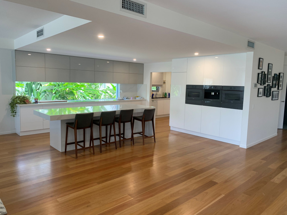 Inspiration for a large modern kitchen in Sunshine Coast with a submerged sink, flat-panel cabinets, white cabinets, engineered stone countertops, black appliances, medium hardwood flooring, an island and white worktops.