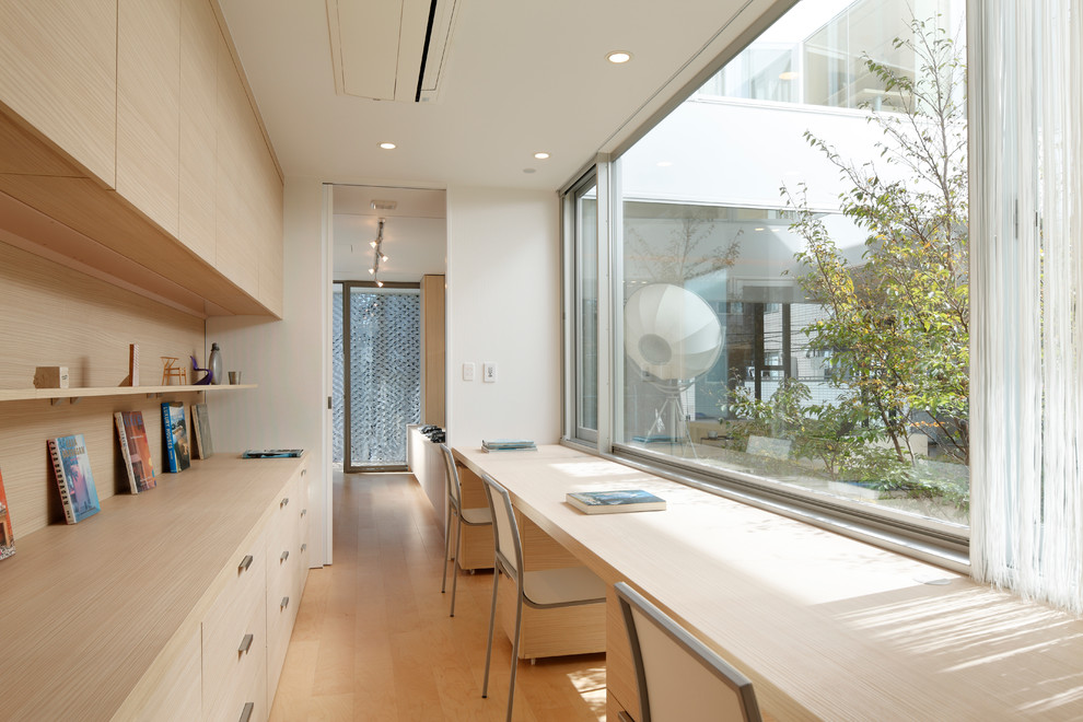Photo of a modern home office in Tokyo with white walls, light hardwood floors, a library and no fireplace.