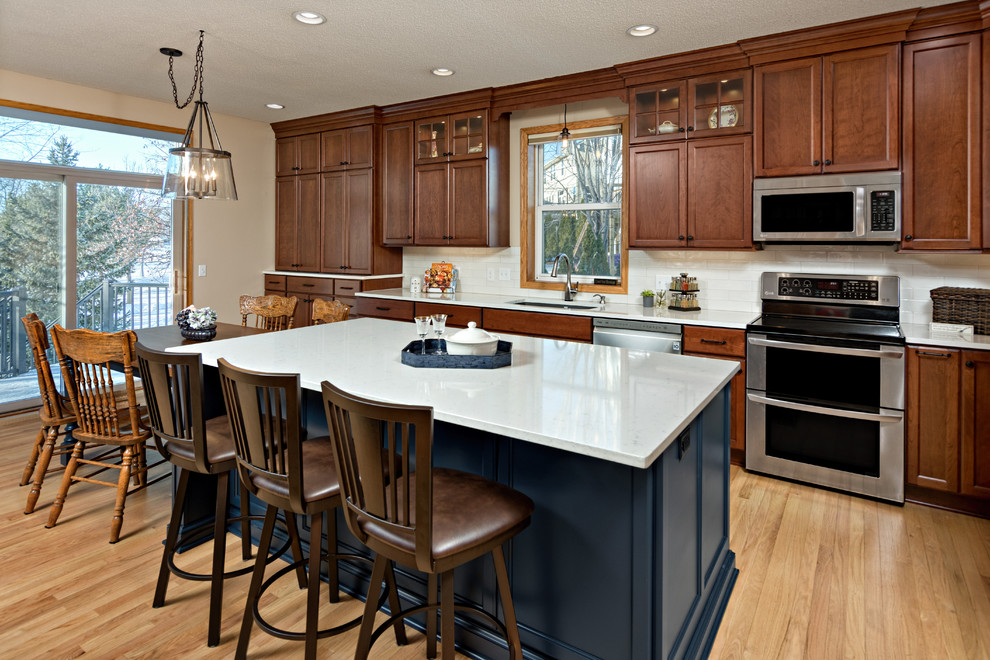 Inspiration for a large traditional l-shaped eat-in kitchen in Minneapolis with an undermount sink, dark wood cabinets, quartz benchtops, white splashback, ceramic splashback, stainless steel appliances, light hardwood floors, white benchtop, with island, recessed-panel cabinets and beige floor.