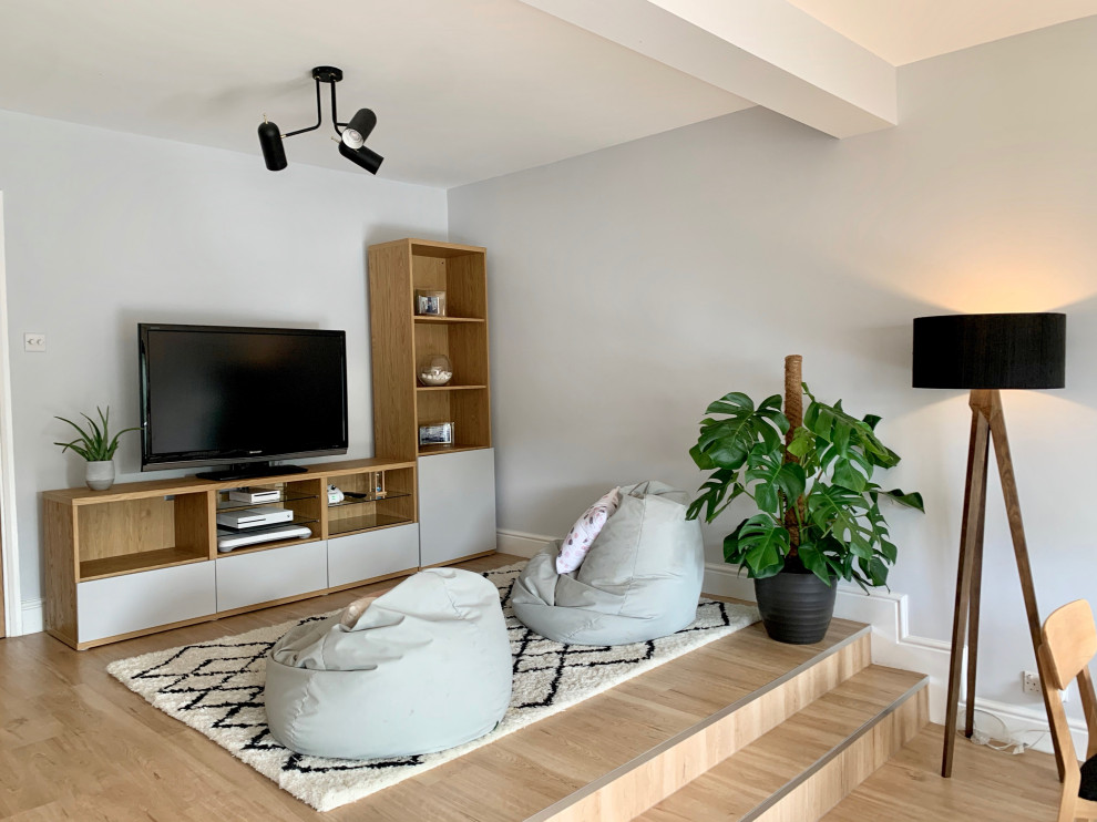 Photo of a large scandinavian open concept living room in Hertfordshire with a library, grey walls, laminate floors, a wood stove, a plaster fireplace surround and a wall-mounted tv.