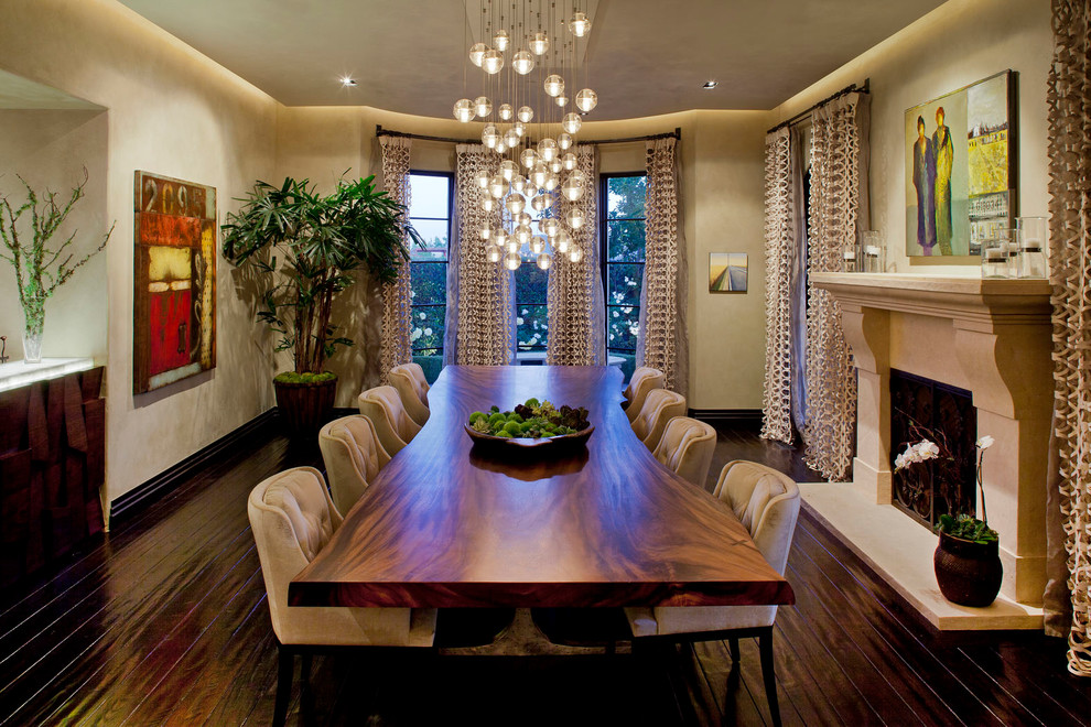 This is an example of a mediterranean separate dining room in Los Angeles with beige walls, dark hardwood floors, a standard fireplace and a plaster fireplace surround.