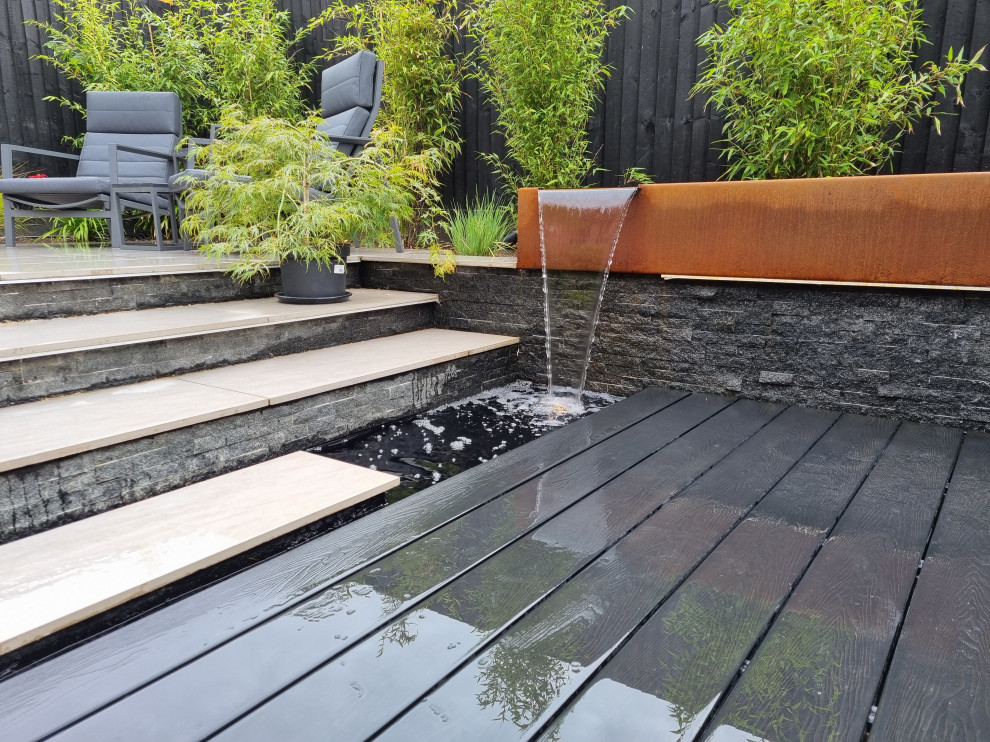 Kleiner, Halbschattiger Moderner Gartenwasserfall im Sommer, hinter dem Haus mit Dielen und Holzzaun in Sonstige