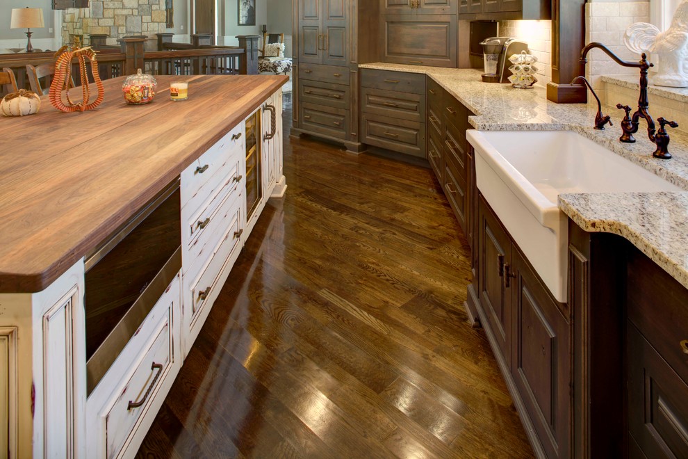 Design ideas for a large country u-shaped kitchen in Kansas City with a farmhouse sink, raised-panel cabinets, dark wood cabinets, granite benchtops, beige splashback, subway tile splashback, panelled appliances, dark hardwood floors and with island.