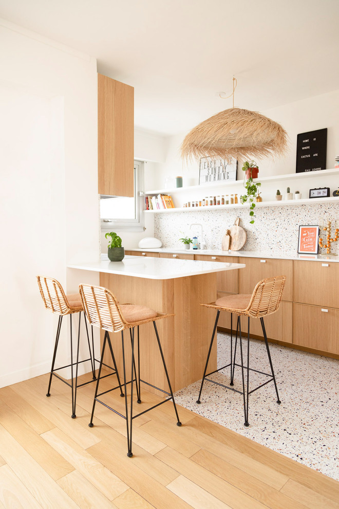 パリにあるお手頃価格の中くらいなコンテンポラリースタイルのおしゃれなキッチン (アンダーカウンターシンク、フラットパネル扉のキャビネット、淡色木目調キャビネット、珪岩カウンター、白いキッチンパネル、石スラブのキッチンパネル、パネルと同色の調理設備、テラゾーの床、白い床、白いキッチンカウンター) の写真