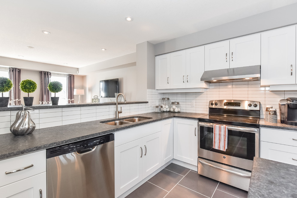 This is an example of a mid-sized transitional l-shaped open plan kitchen in Toronto with an undermount sink, shaker cabinets, white cabinets, granite benchtops, white splashback, ceramic splashback, stainless steel appliances, porcelain floors and with island.