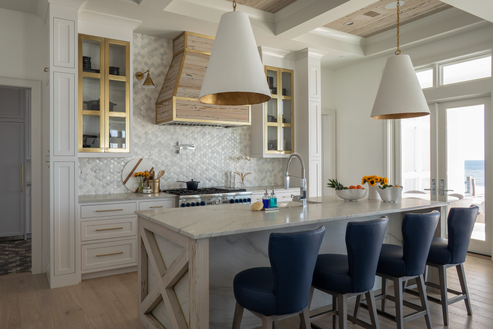 Example of a large beach style l-shaped light wood floor, beige floor and coffered ceiling open concept kitchen design in Other with a farmhouse sink, glass-front cabinets, white cabinets, marble countertops, gray backsplash, ceramic backsplash, stainless steel appliances, an island and white countertops