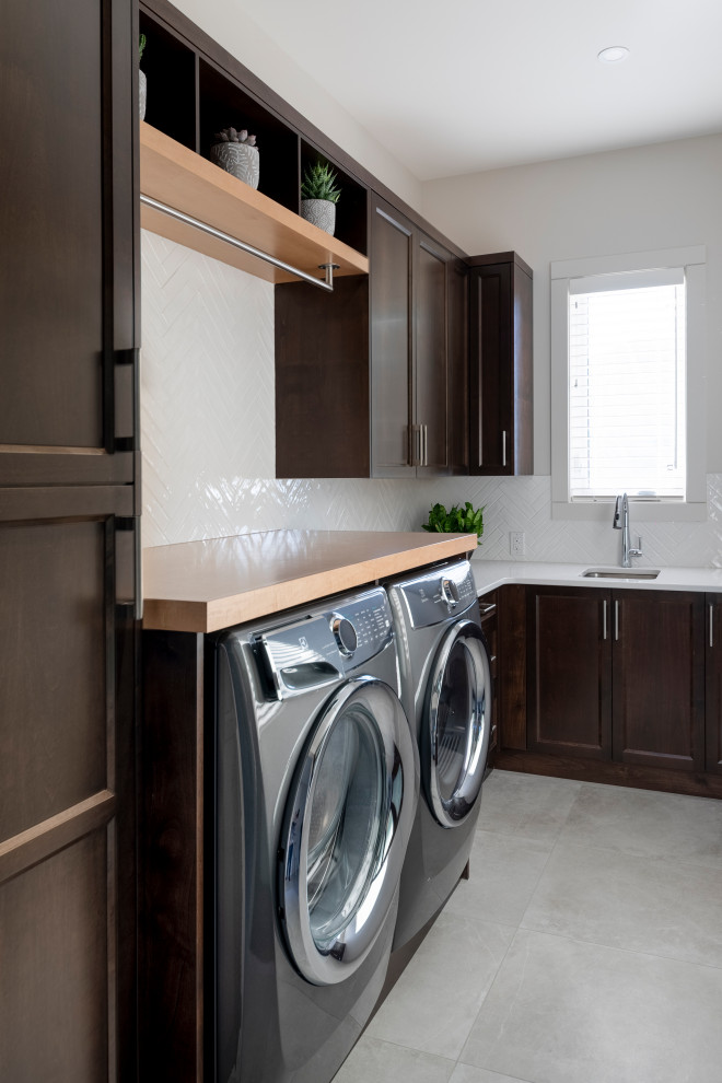Inspiration for a mid-sized transitional l-shaped dedicated laundry room in Vancouver with an undermount sink, recessed-panel cabinets, dark wood cabinets, white splashback, subway tile splashback, white walls, a side-by-side washer and dryer, grey floor and white benchtop.