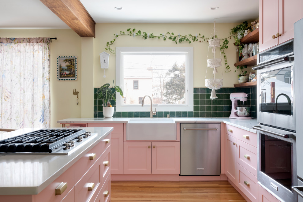 Photo of a mid-sized eclectic l-shaped eat-in kitchen in Minneapolis with a farmhouse sink, shaker cabinets, pink cabinets, quartz benchtops, green splashback, terra-cotta splashback, stainless steel appliances, light hardwood floors, with island, beige floor and white benchtop.