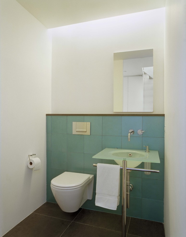 This is an example of a small modern 3/4 bathroom in New York with a wall-mount toilet, blue tile, glass tile, blue walls, cement tiles, a pedestal sink, glass benchtops, grey floor and blue benchtops.