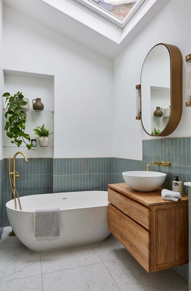 Photo of a mid-sized transitional kids bathroom in London with medium wood cabinets, a freestanding tub, an open shower, a wall-mount toilet, green tile, ceramic tile, white walls, marble floors, a vessel sink, wood benchtops, white floor, a hinged shower door, brown benchtops, a niche, a single vanity, a floating vanity and vaulted.