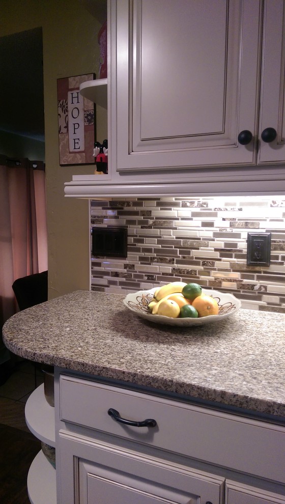 Eat-in kitchen - mid-sized transitional l-shaped laminate floor eat-in kitchen idea with an undermount sink, raised-panel cabinets, white cabinets, granite countertops, multicolored backsplash, mosaic tile backsplash, white appliances and no island