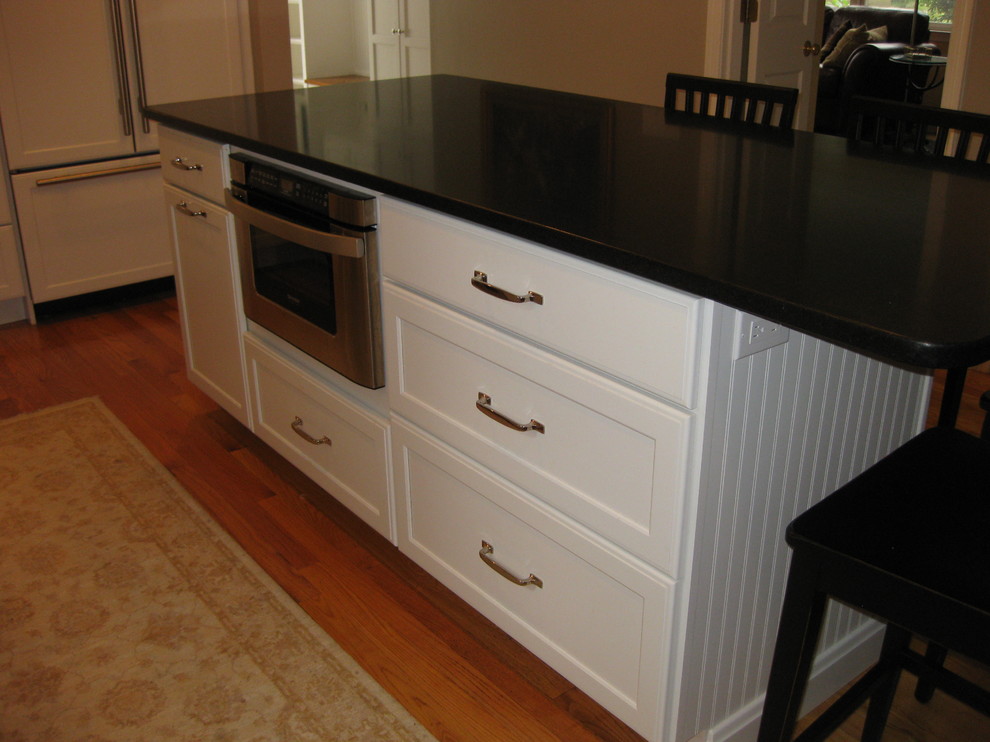 Example of a transitional u-shaped medium tone wood floor eat-in kitchen design in Boston with an undermount sink, recessed-panel cabinets, white cabinets, gray backsplash, subway tile backsplash, stainless steel appliances, an island and black countertops