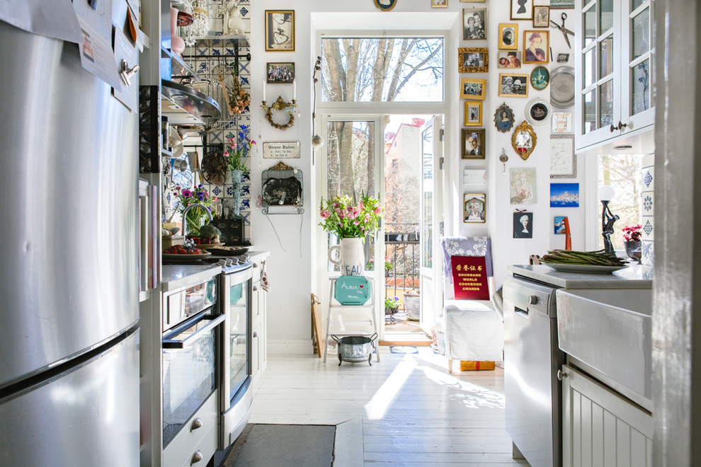 This is an example of a mid-sized eclectic galley kitchen in Stockholm with white cabinets, marble benchtops, stainless steel appliances and painted wood floors.