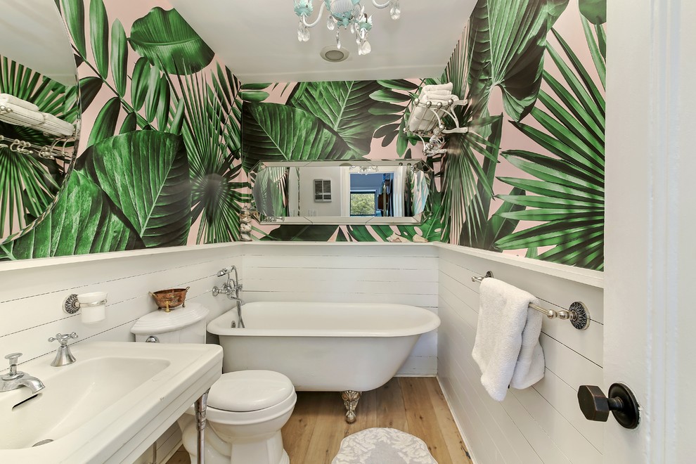 Photo of a mid-sized tropical master bathroom in New York with a freestanding tub, a two-piece toilet, white tile, white walls, light hardwood floors, a pedestal sink and beige floor.
