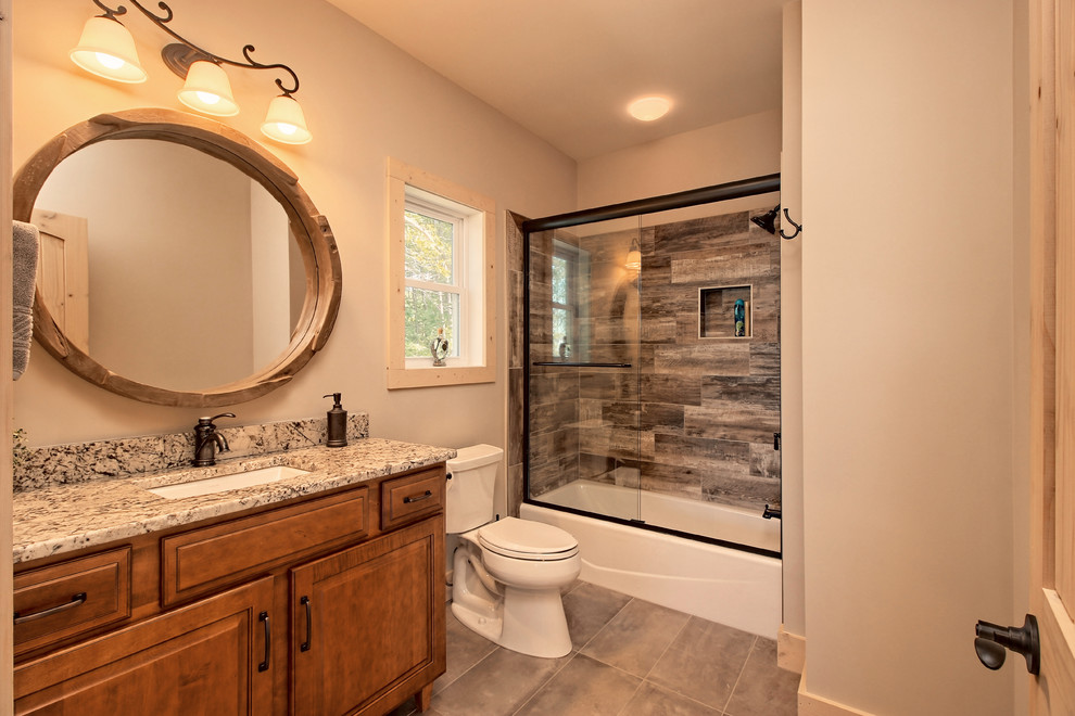 This is an example of a mid-sized arts and crafts bathroom in Atlanta with raised-panel cabinets, medium wood cabinets, an alcove tub, an alcove shower, a two-piece toilet, multi-coloured tile, ceramic tile, beige walls, ceramic floors, an undermount sink, granite benchtops, brown floor, a sliding shower screen and multi-coloured benchtops.