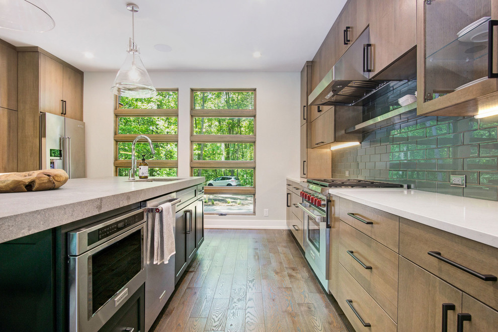 Example of a mountain style medium tone wood floor kitchen design in Grand Rapids with an undermount sink, flat-panel cabinets, quartz countertops, green backsplash, glass tile backsplash and stainless steel appliances