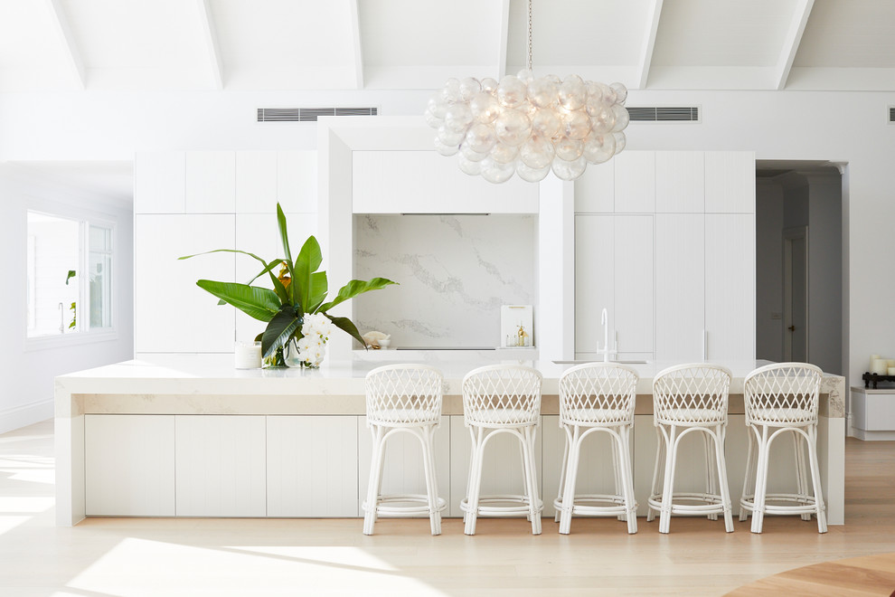 Photo of a large beach style galley eat-in kitchen in Sydney with an undermount sink, white cabinets, white splashback, panelled appliances, with island, white benchtop, light hardwood floors and beige floor.