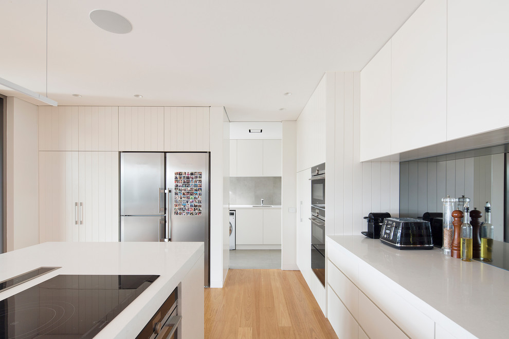 Photo of a large modern l-shaped open plan kitchen in Sydney with an undermount sink, flat-panel cabinets, white cabinets, quartz benchtops, mirror splashback, stainless steel appliances, medium hardwood floors, with island and brown floor.