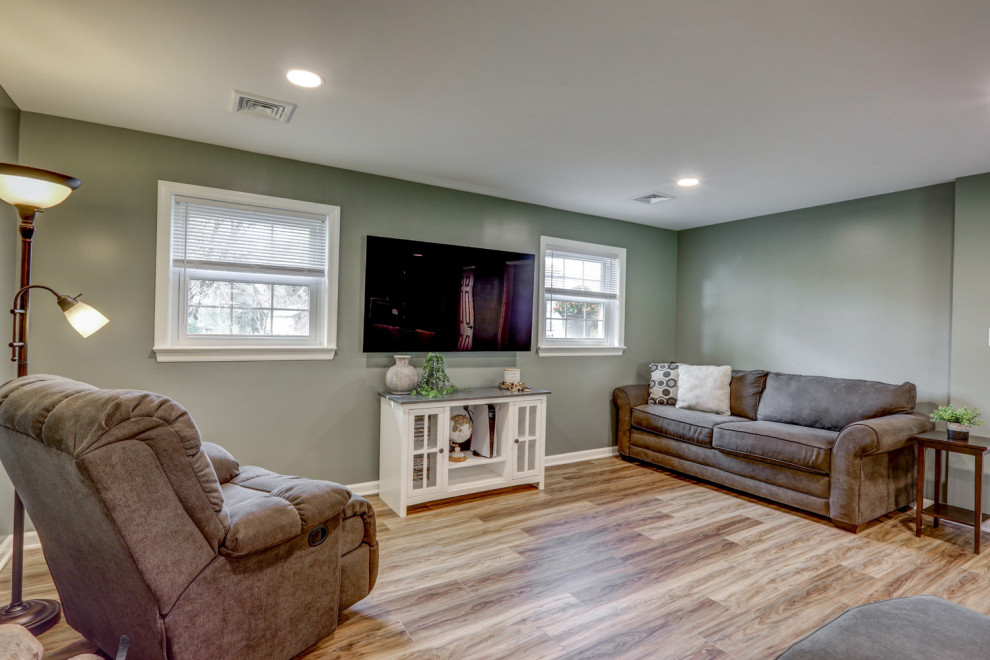 This is an example of a large traditional walk-out basement in Other with green walls, vinyl flooring, a standard fireplace, a brick fireplace surround and brown floors.
