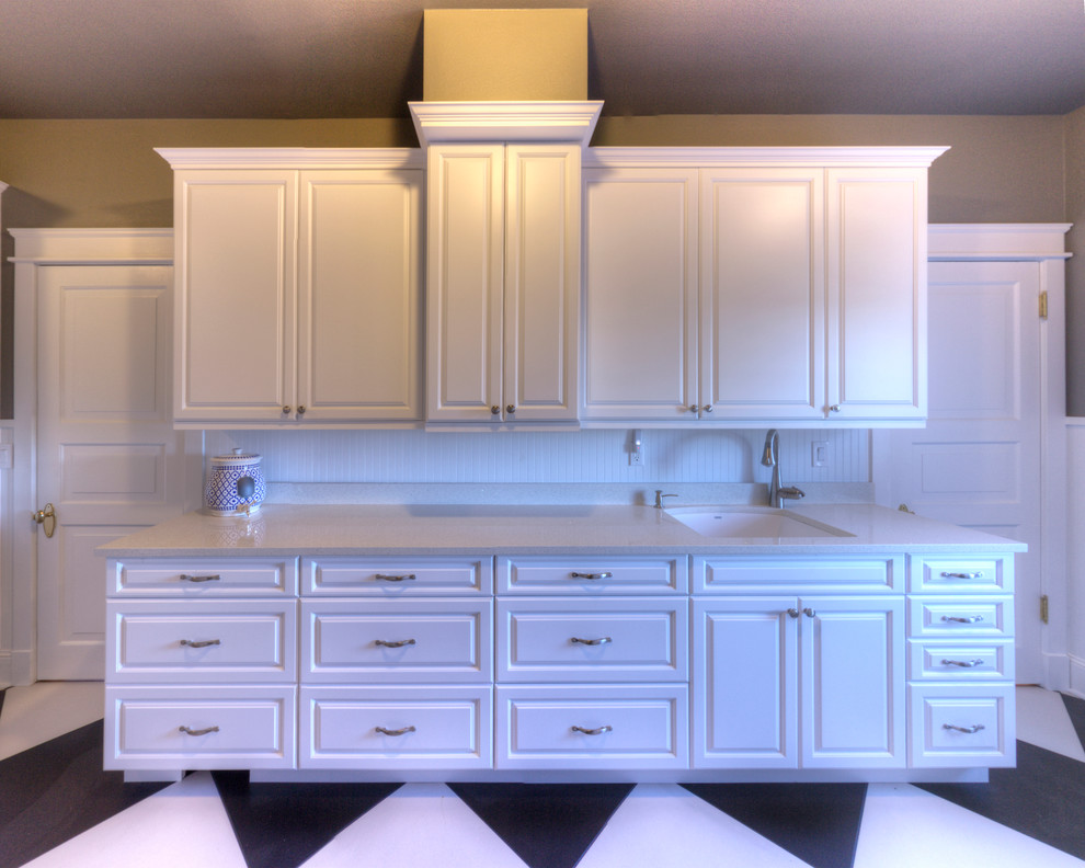 This is an example of a traditional laundry room in Seattle with a single-bowl sink, grey walls, raised-panel cabinets, white cabinets, quartz benchtops and a side-by-side washer and dryer.