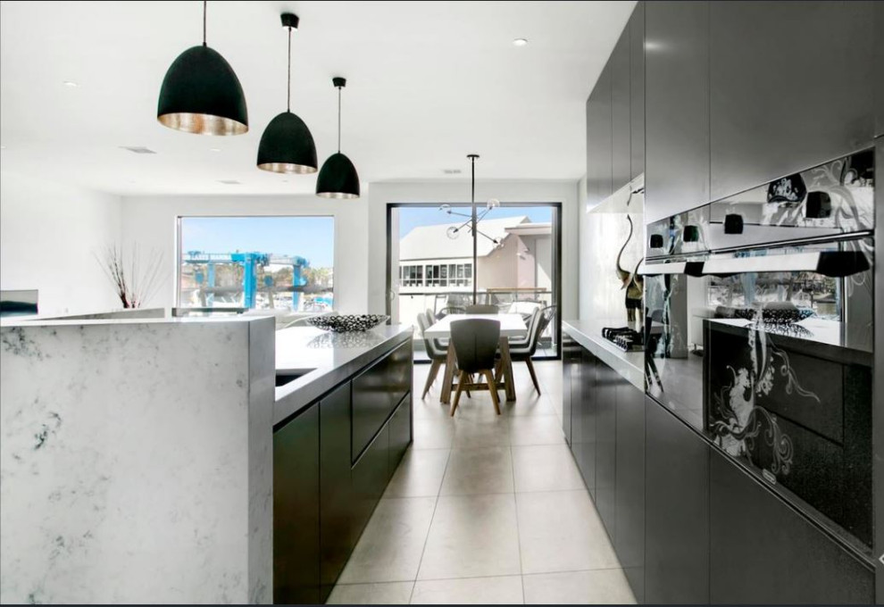 Photo of a small contemporary galley eat-in kitchen in Melbourne with flat-panel cabinets, quartz benchtops, with island, an undermount sink, black cabinets, white splashback, stone slab splashback, black appliances, porcelain floors, grey floor and yellow benchtop.