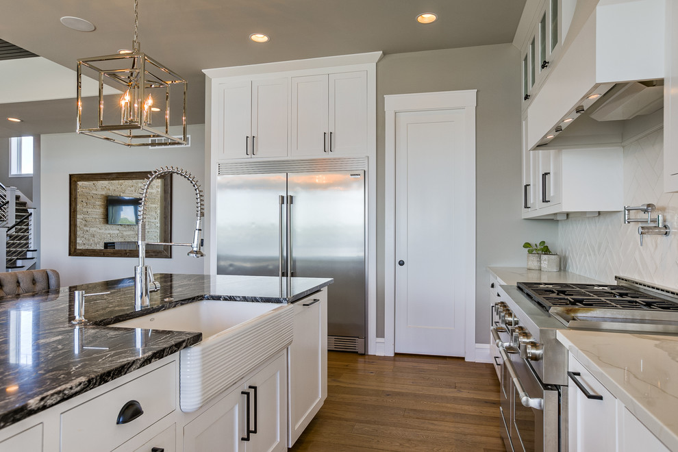 Inspiration for a beach style open plan kitchen in Omaha with a farmhouse sink, shaker cabinets, white cabinets, white splashback, stainless steel appliances, light hardwood floors and with island.