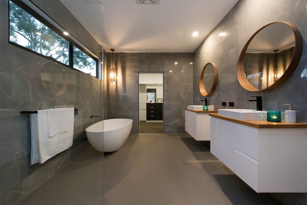 Inspiration for a contemporary master bathroom in Brisbane with flat-panel cabinets, white cabinets, a freestanding tub, a corner shower, gray tile, grey walls, a vessel sink, wood benchtops, grey floor, an open shower and brown benchtops.