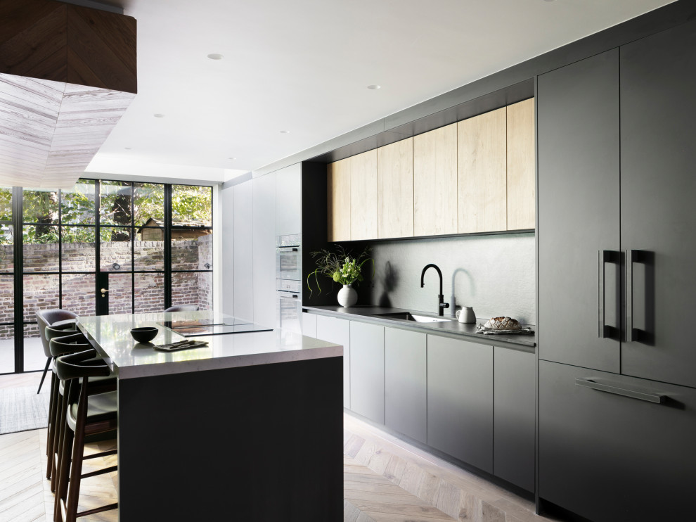 Mid-sized contemporary galley eat-in kitchen in London with an integrated sink, flat-panel cabinets, black cabinets, solid surface benchtops, black splashback, engineered quartz splashback, black appliances, light hardwood floors, with island, brown floor, black benchtop and recessed.