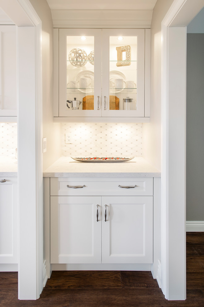 Example of a mid-sized transitional single-wall dark wood floor and brown floor kitchen design in Toronto with recessed-panel cabinets, white cabinets, quartz countertops, white backsplash, ceramic backsplash, stainless steel appliances and white countertops