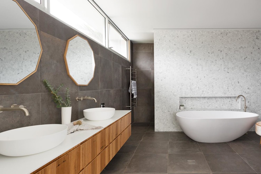Photo of a large contemporary master wet room bathroom in Sydney with medium wood cabinets, a freestanding tub, a one-piece toilet, gray tile, marble, grey walls, porcelain floors, a vessel sink, black floor, an open shower and white benchtops.