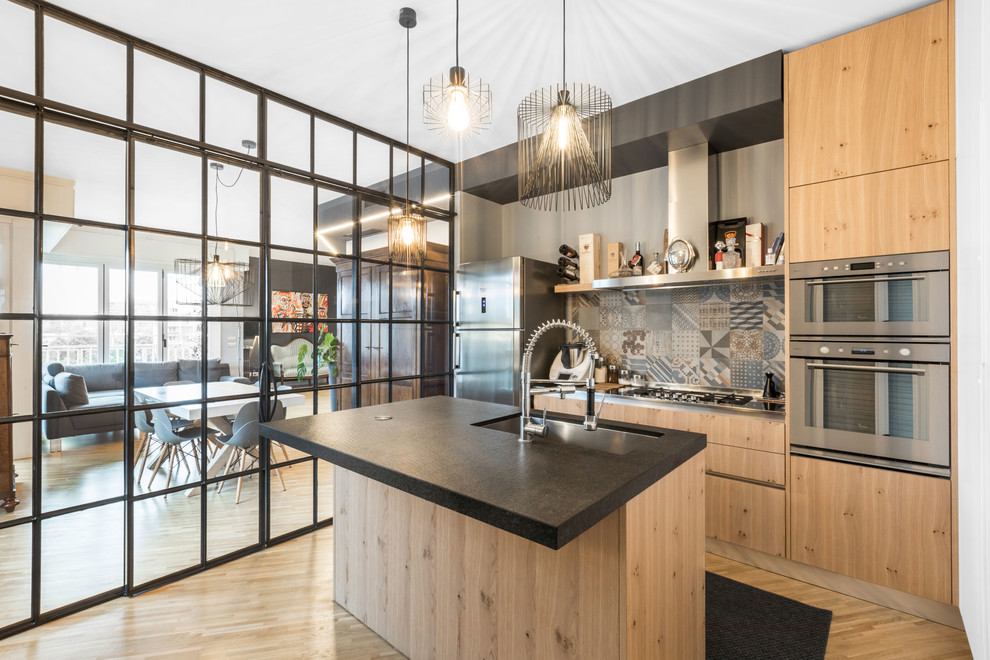 Inspiration for a contemporary galley kitchen in Milan with an undermount sink, flat-panel cabinets, medium wood cabinets, multi-coloured splashback, stainless steel appliances, medium hardwood floors, with island, brown floor and black benchtop.
