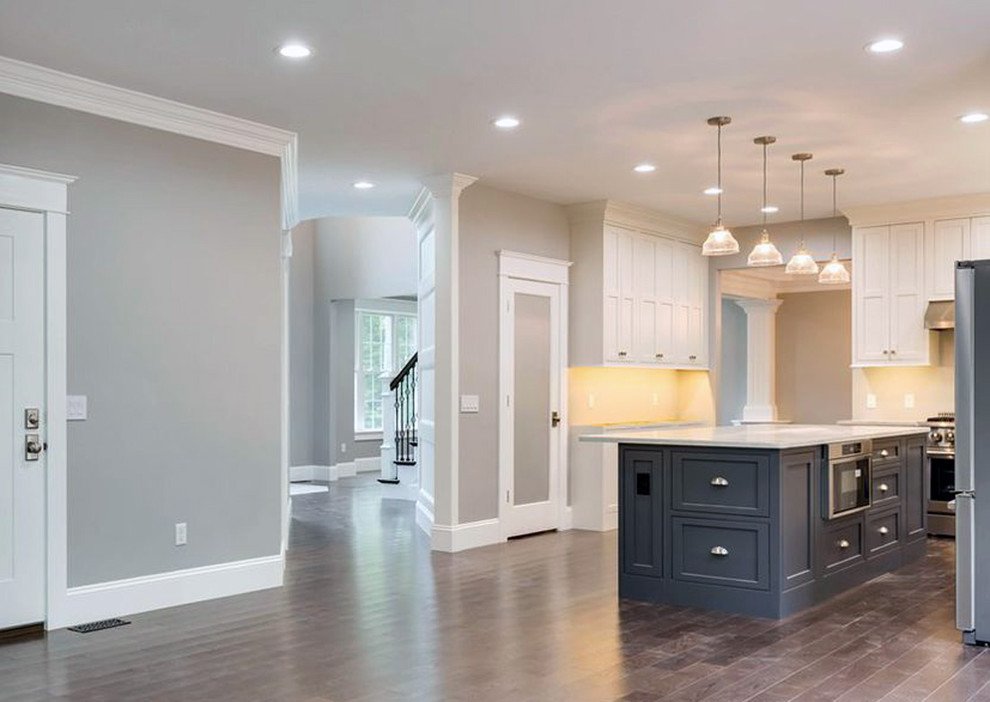 Inspiration for a large transitional l-shaped dark wood floor and brown floor kitchen pantry remodel with a farmhouse sink, recessed-panel cabinets, white cabinets, quartz countertops, stainless steel appliances, an island and white countertops