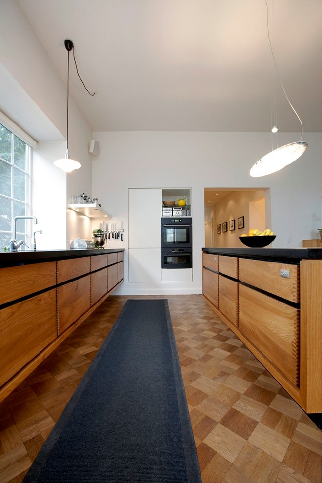 Inspiration for a large scandinavian galley open plan kitchen in Copenhagen with flat-panel cabinets, medium wood cabinets, medium hardwood floors, with island, a drop-in sink and black appliances.