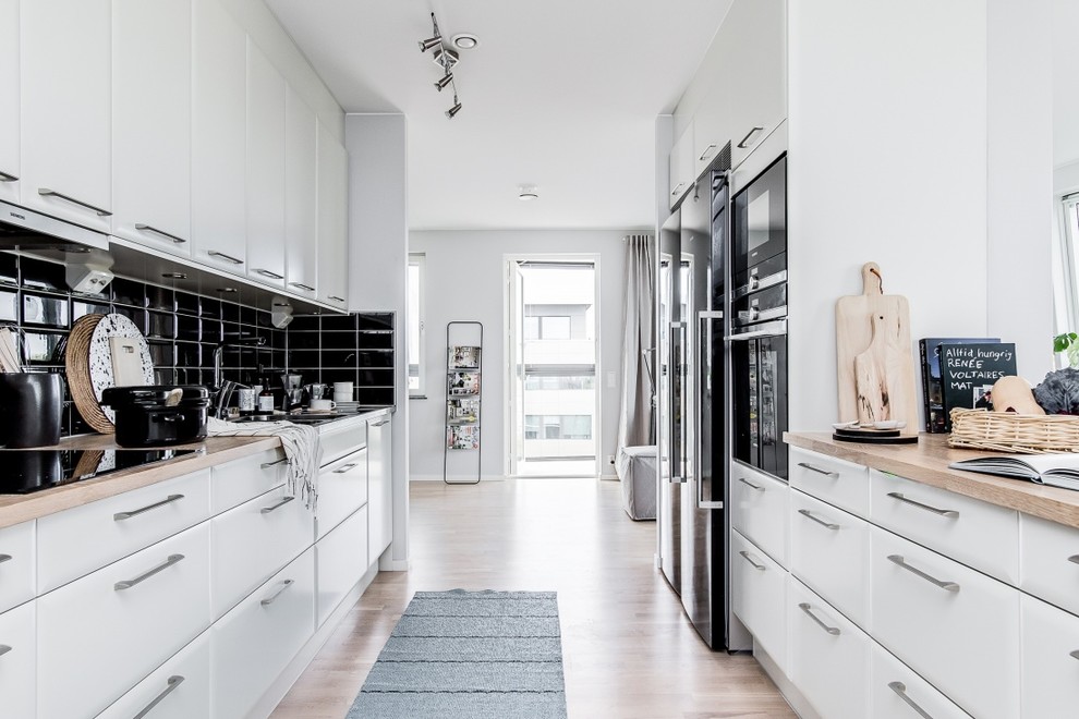 Design ideas for a mid-sized scandinavian galley separate kitchen in Stockholm with wood benchtops and black splashback.