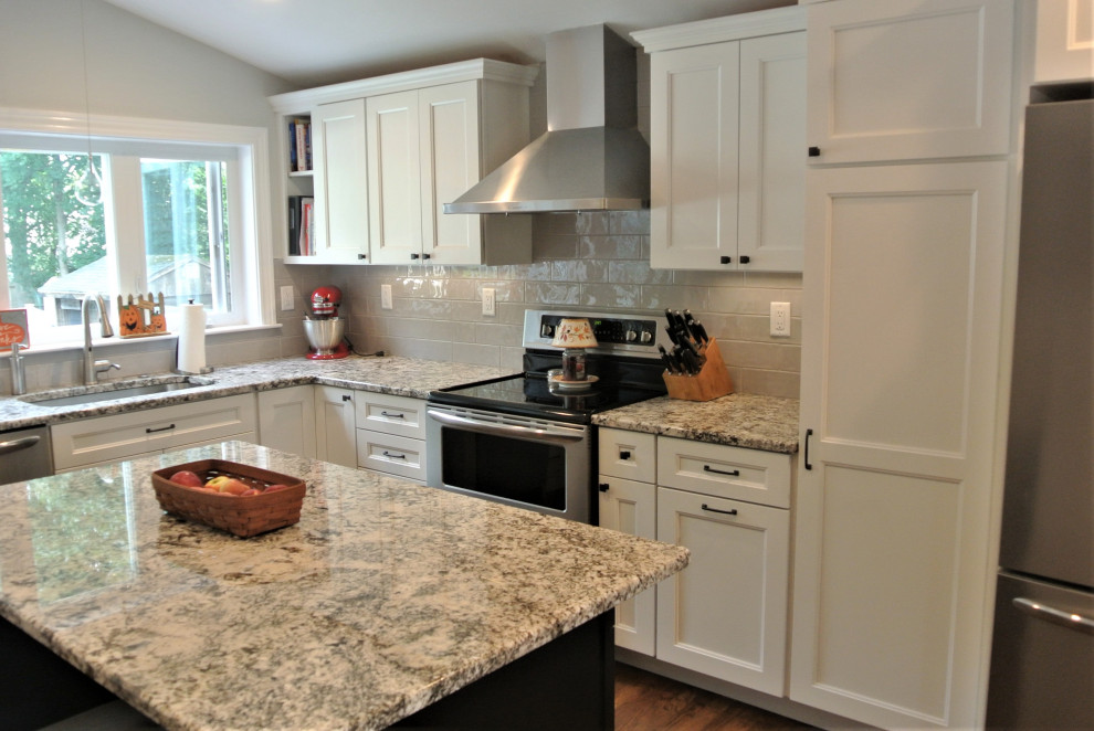 Example of a transitional l-shaped medium tone wood floor and brown floor eat-in kitchen design in Boston with an undermount sink, shaker cabinets, white cabinets, granite countertops, beige backsplash, subway tile backsplash, stainless steel appliances, an island and beige countertops