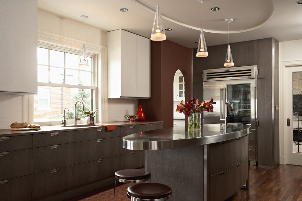 This is an example of a large contemporary l-shaped kitchen in Minneapolis with stainless steel benchtops, an undermount sink, flat-panel cabinets, white splashback, stainless steel appliances, dark hardwood floors, with island, subway tile splashback, grey cabinets and brown floor.