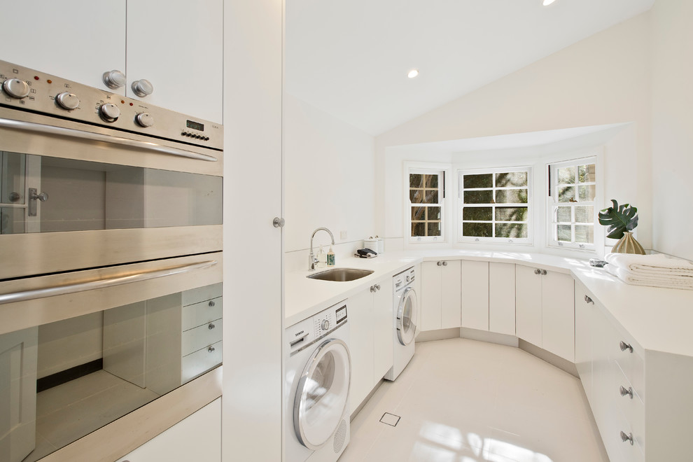 Photo of a contemporary u-shaped utility room in Sydney with an undermount sink, flat-panel cabinets, white cabinets, white walls and a side-by-side washer and dryer.