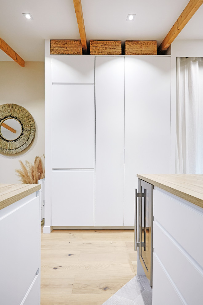This is an example of a mid-sized scandinavian gender-neutral built-in wardrobe in Paris with raised-panel cabinets, white cabinets, light hardwood floors, beige floor and exposed beam.