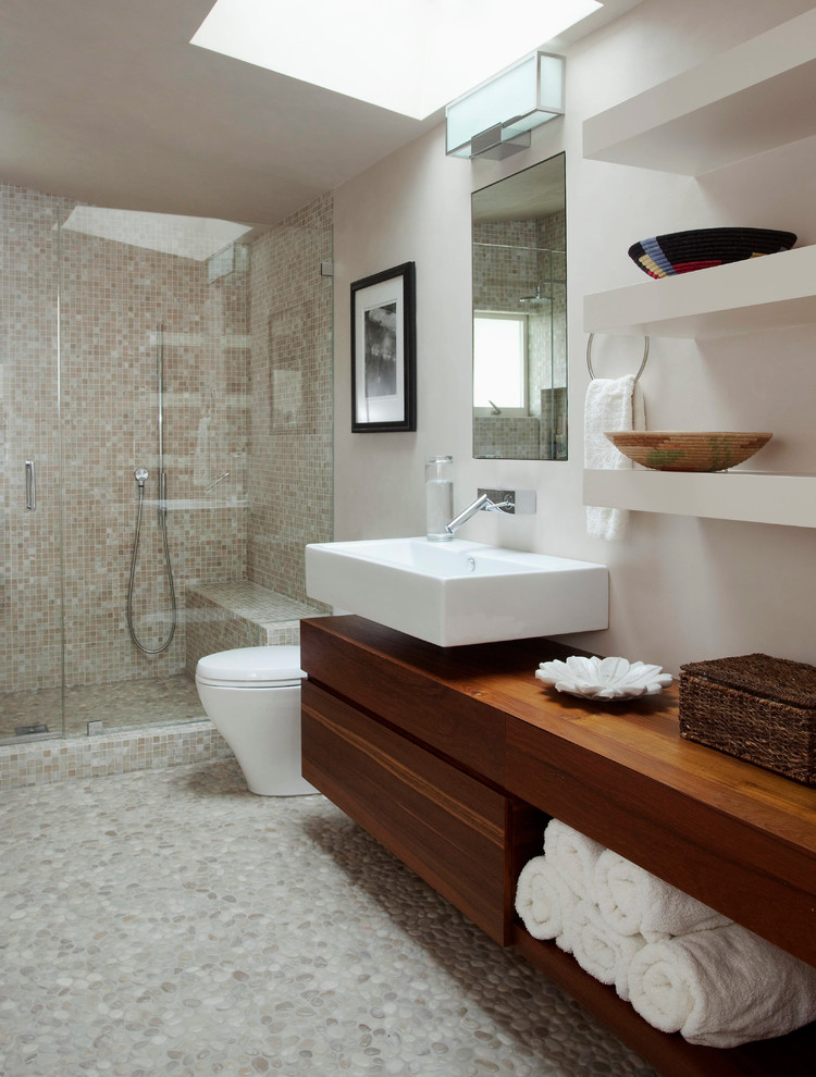 This is an example of a large contemporary 3/4 bathroom in New York with a wall-mount sink, flat-panel cabinets, dark wood cabinets, an alcove shower, beige tile, mosaic tile, white walls, pebble tile floors, wood benchtops, grey floor, a hinged shower door and brown benchtops.