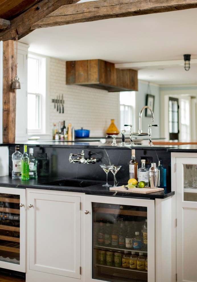 Design ideas for a mid-sized country single-wall wet bar in Boston with an integrated sink, white cabinets, black splashback, medium hardwood floors and shaker cabinets.