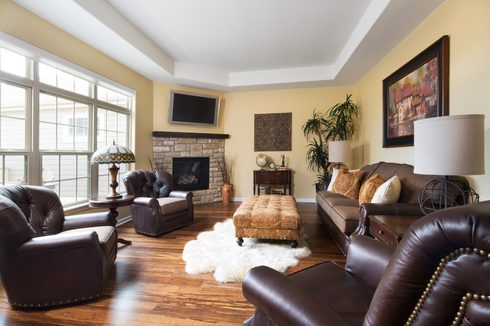 Large traditional enclosed family room in Milwaukee with yellow walls, medium hardwood floors, a corner fireplace, a stone fireplace surround and a wall-mounted tv.