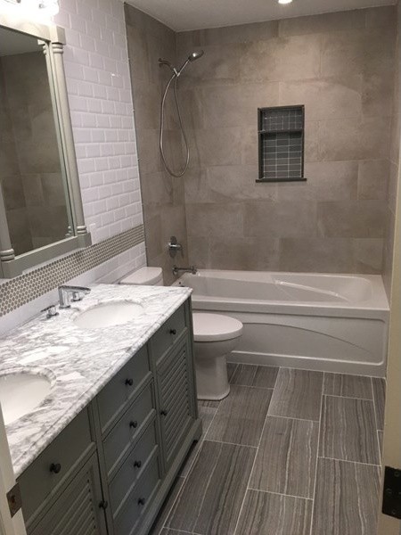 Inspiration for a mid-sized transitional master bathroom in New York with grey cabinets, a corner tub, a shower/bathtub combo, white tile, ceramic tile, white walls, ceramic floors, a drop-in sink, marble benchtops, flat-panel cabinets, a two-piece toilet, grey floor and a shower curtain.