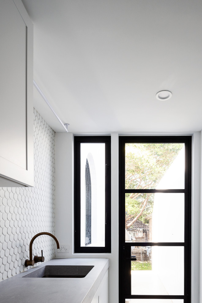 Idéer för funkis parallella grått tvättstugor, med en integrerad diskho, luckor med infälld panel, vita skåp, bänkskiva i betong, vitt stänkskydd, stänkskydd i mosaik, betonggolv, tvättmaskin och torktumlare byggt in i ett skåp och grått golv